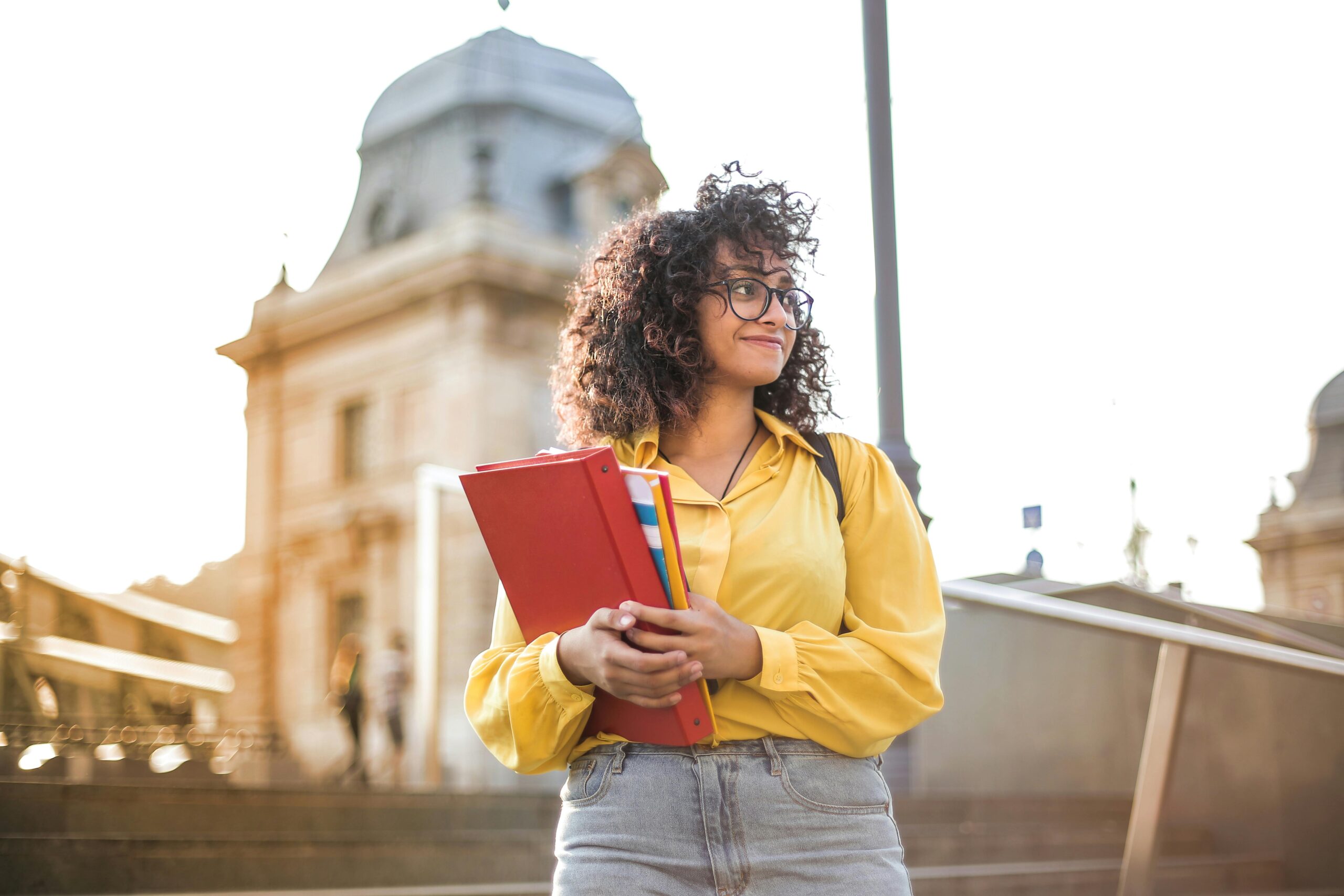 Studentessa in piedi che sorride con libri e quaderni in mano